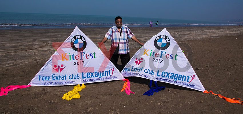 Two large white delta kites printed with BMW KiteFest 2017 and Pune Expat Club branding on a beach, with a person standing behind them